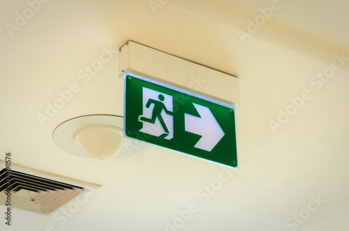 green emergency fire exit sign on ceiling in office building or shopping mall