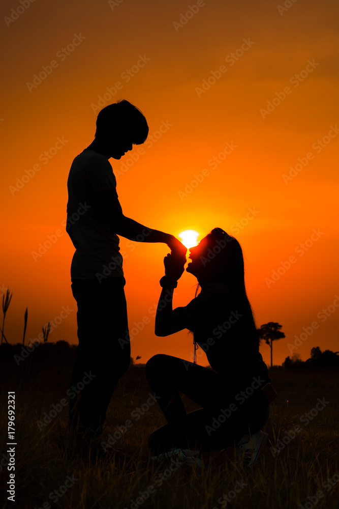 Silhouette of a romantic couple on beauty sunset. Women kneels kissing a boyfriend's hand.
