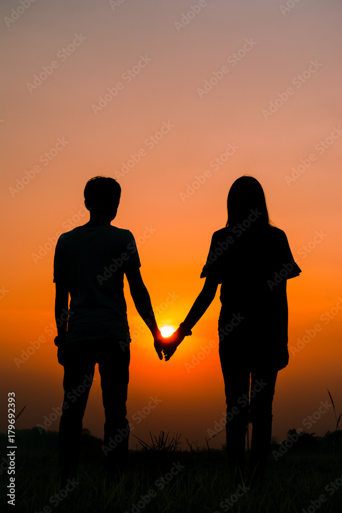 Silhouette of a couple standing and holding hand on sunset.