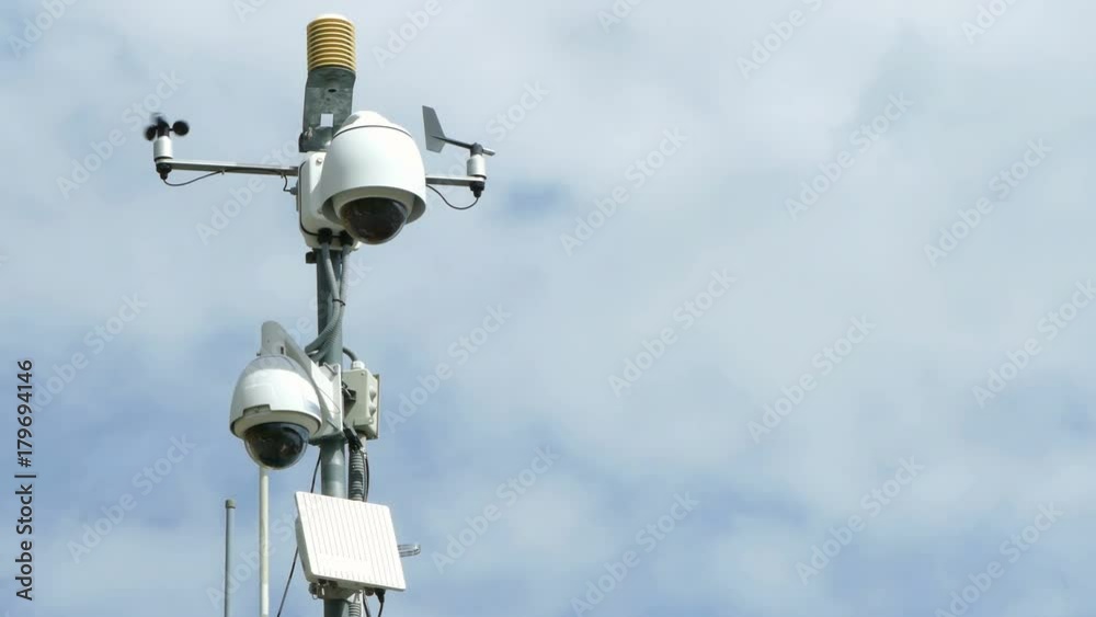 Security Cameras. Pole with video surveillance system, vane and anemometer,with blue sky and clouds background.
