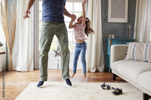 Girl and dad jumping up holding hands, her arm in the air