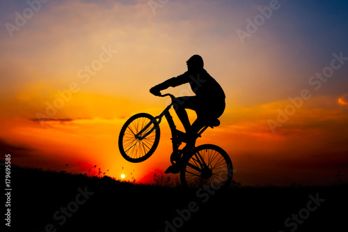 Boy riding bicycle on background sunset.