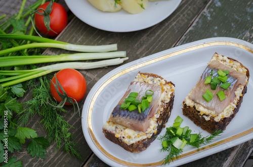 Herring, green onions, butter, French mustard and a slice of rye bread on an old wooden table.