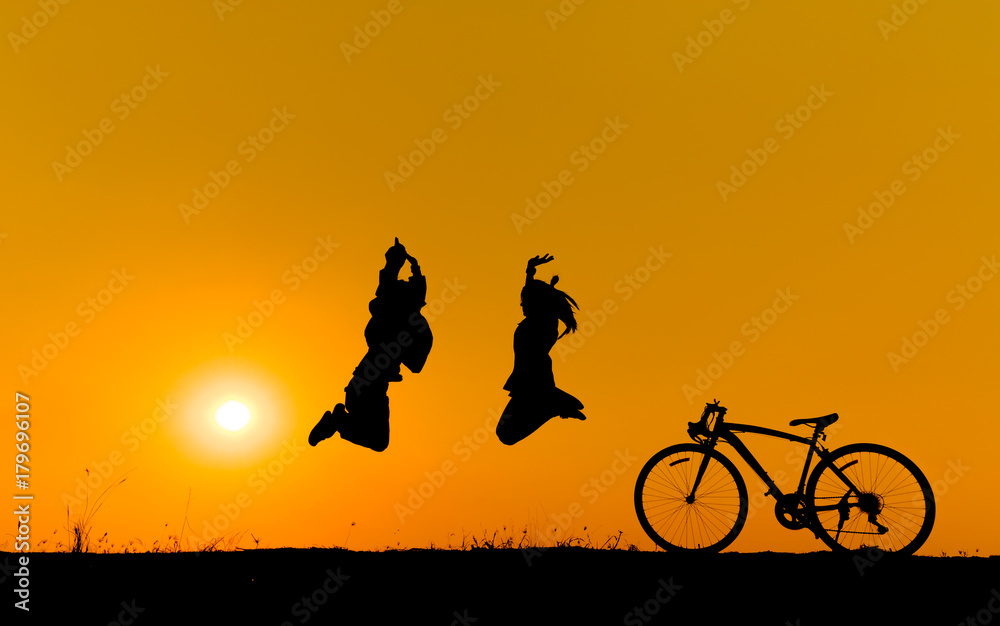 Silhouette of a children jumping on grass with a bicycle.