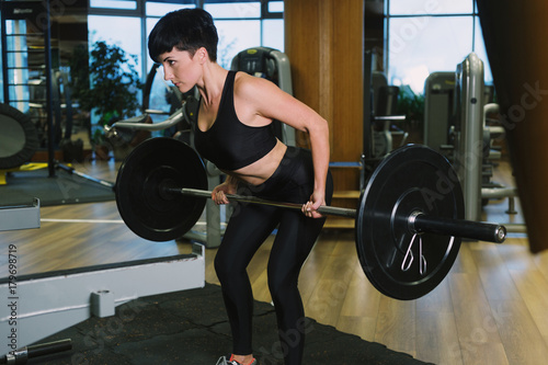 Fit young woman lifting barbells looking focused, working out in a gym, doing barbell row