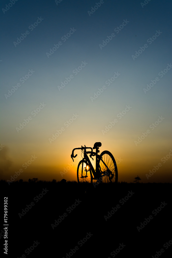 Obraz premium silhouette of a bicycle against a bright orange and blue sunset.