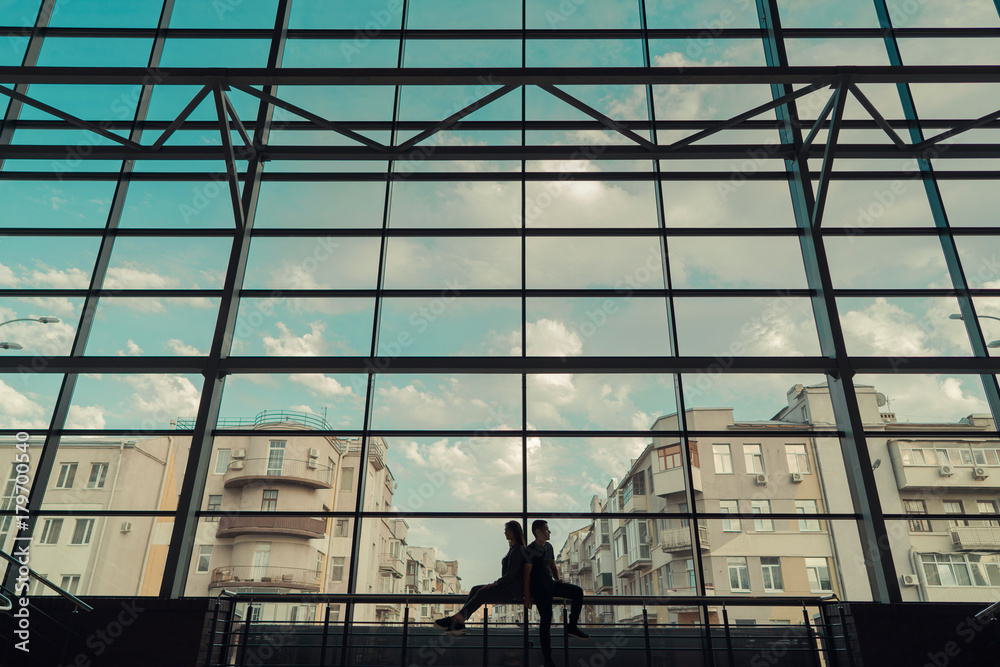 silhouette of a couple sitting back to back near a huge window on the background of the city and streets, wide angle