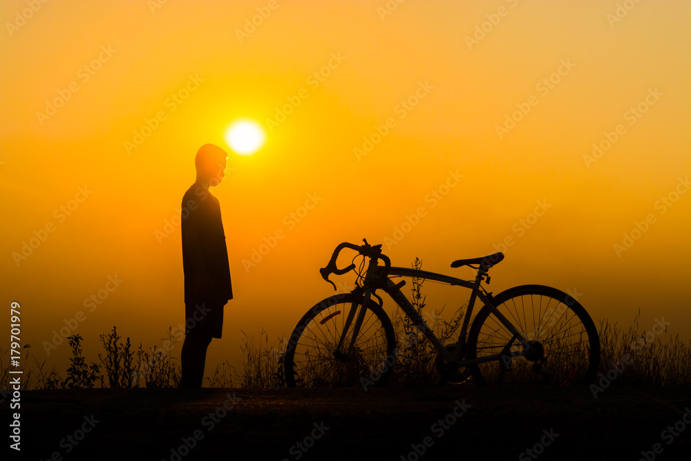 Obraz premium a person standing next to a bicycle, silhouetted against a bright orange sunset.