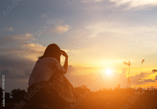 Silhouette of woman praying over beautiful sky background