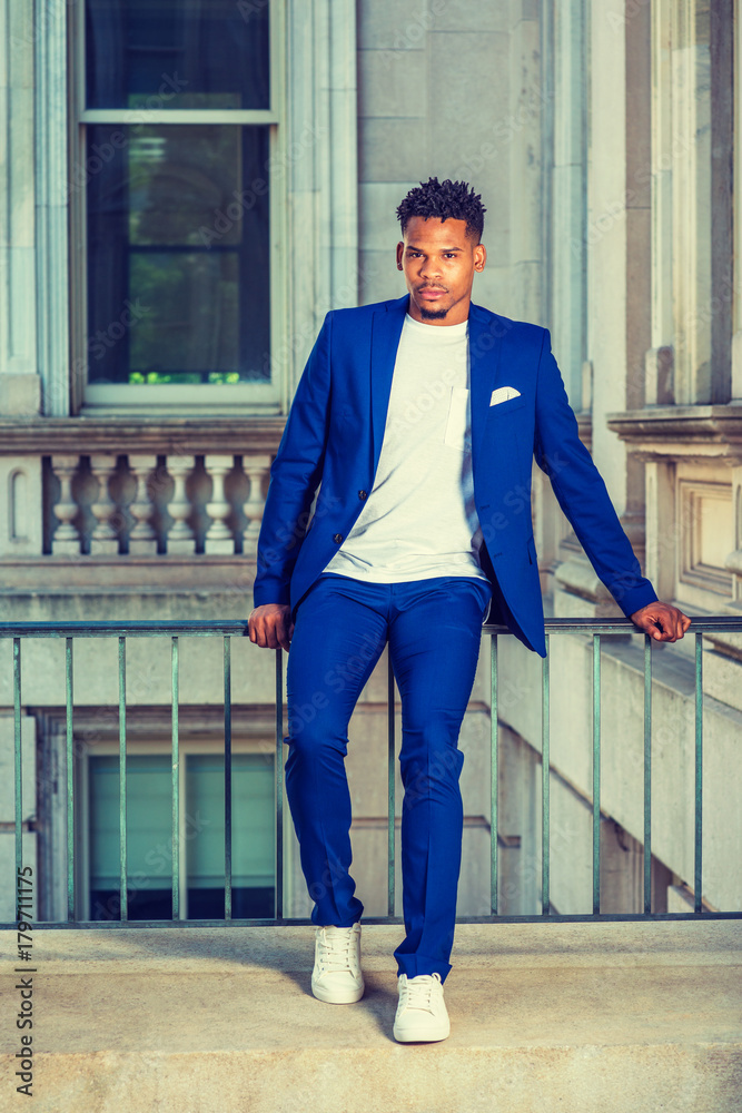 African American college student studying in New York, wearing blue suit,  white T shirt, sneakers, sitting on railing in vintage office building on  campus, taking break. Instagram filtered effect.. Photos | Adobe