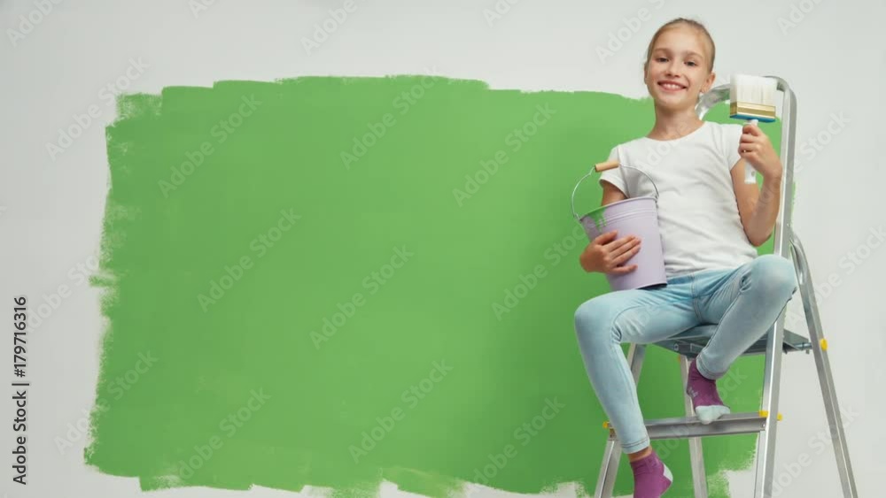 Child sitting on ladder with bucket of paint and a brush in her hand
