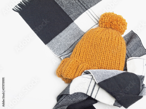 Mustard knit beanie hat with big pom pom and black and white checked scarf isolated on white background. Copy space. Flat lay. Top view