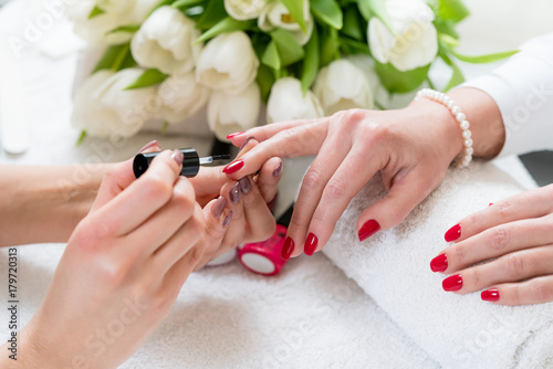 Hands of a skilled manicurist applying red nail polish on the nails of a young woman