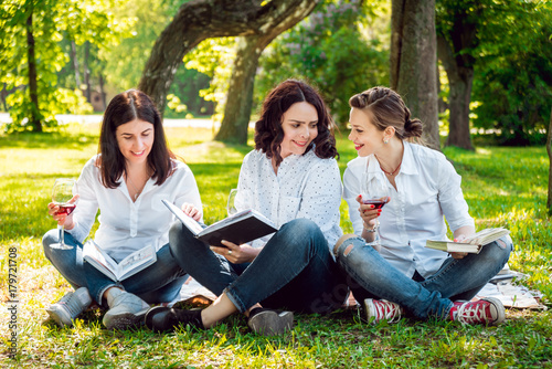 Young beautiful girls with glass of red wine and books in the park.
