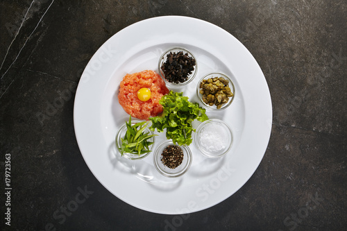 Tartar with salmon with divided ingredients in jars on black background