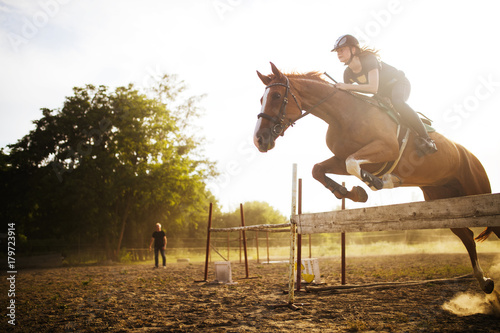 Young female jockey on horse leaping over hurdle photo