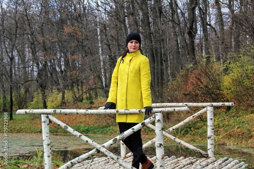 A woman in a yellow coat is standing on a birch bridge in the estate of Count Leo Tolstoy in Yasnaya Polyana.