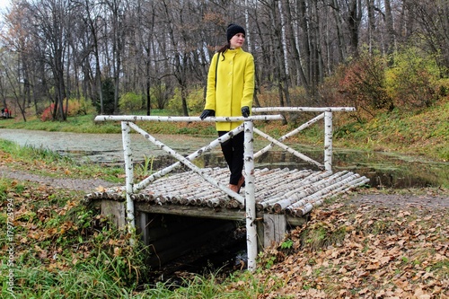A woman in a yellow coat is standing on a birch bridge in the estate of Count Leo Tolstoy in Yasnaya Polyana.