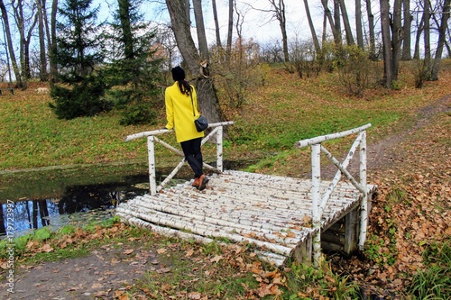 A woman in a yellow coat is standing on a birch bridge in the estate of Count Leo Tolstoy in Yasnaya Polyana.