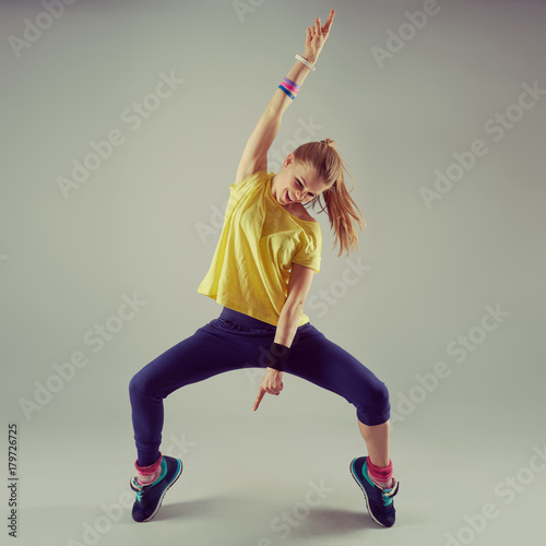 Portrait of active girl performing aerobics dance over grey background. Sport and leisure concept. 