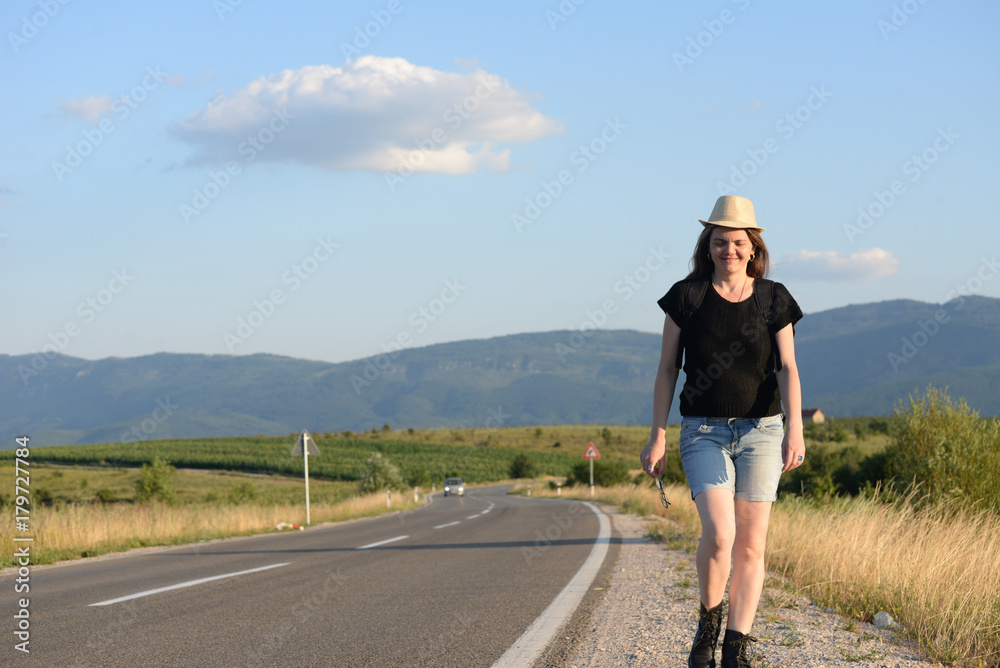 Naklejka premium Woman Walking on the road in mountains at sunset. Forty Years old woman on the road