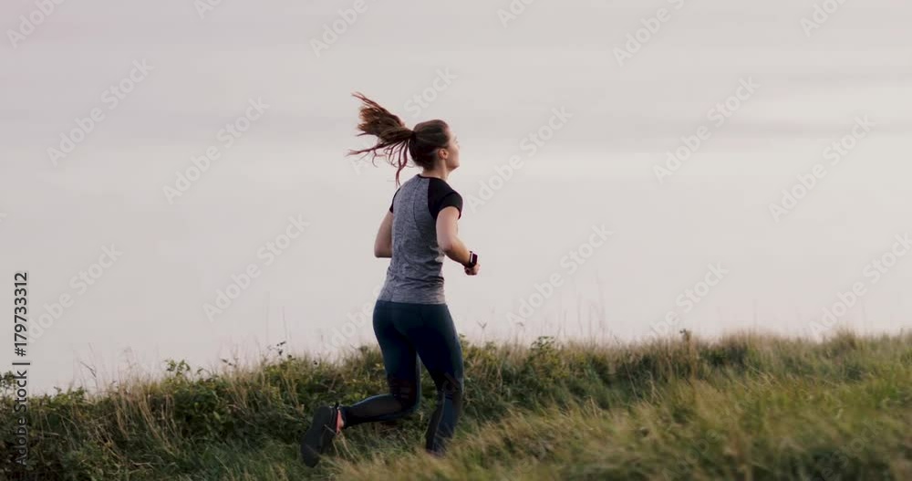 Active young adult female running on cliff by sea Active young adult female running on cliff by sea