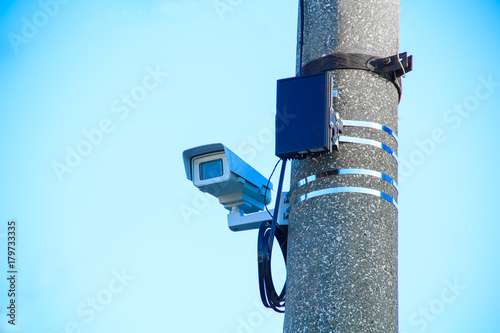 The video camera in the sealed thermal jacket on the bracket is fixed on a metal road pillar next to the infrared searchlight to monitor traffic violations.