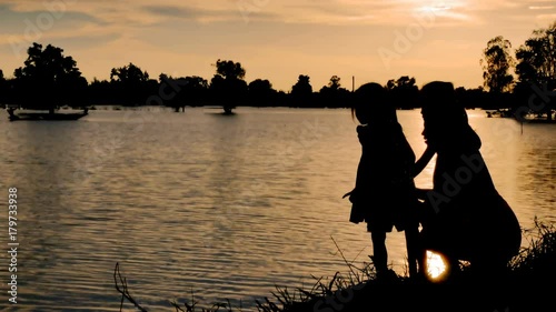 Silhouette of happy family, mother and daughter playing and throwing rock into the river together at sunset. 