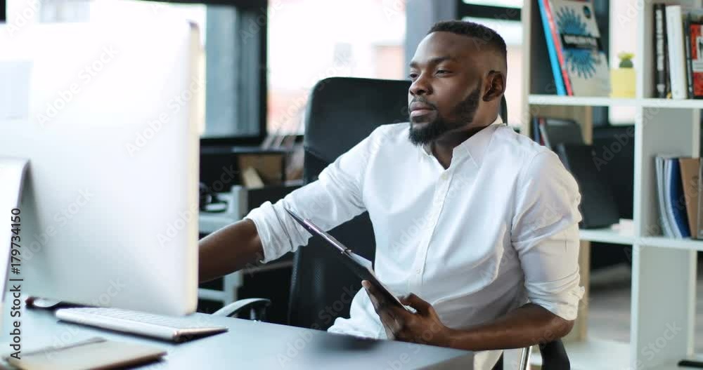 Serious african american working in office using a computer writes documents focused on work looking in monitor screen technology businessman casual communication successful portrait Slow Motion Shot