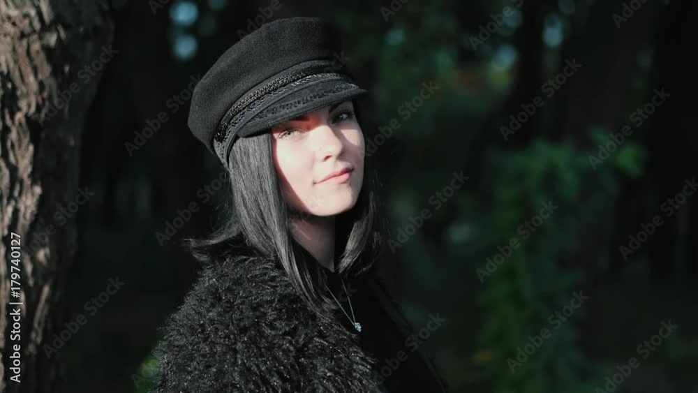 Naturally beautiful brunette trendy girl in autumn park. Portrait of woman in fashion black cap looking into camera and smiling. Slow motion. Naturally beautiful brunette trendy girl in autumn park. Portrait of woman in fashion black cap looking into camera and smiling. Slow motion.