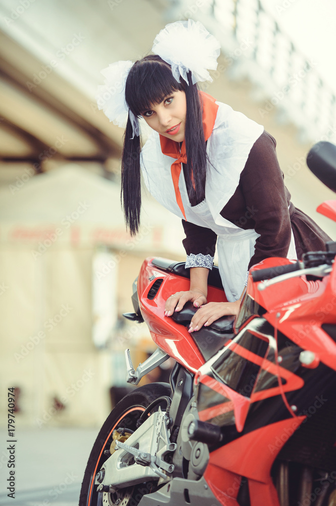 Beautiful young woman, hairstyle and bows outdoors with a motorcycle. Happy and healthy dressed in a Soviet school uniform. girl biker. Concept of fun