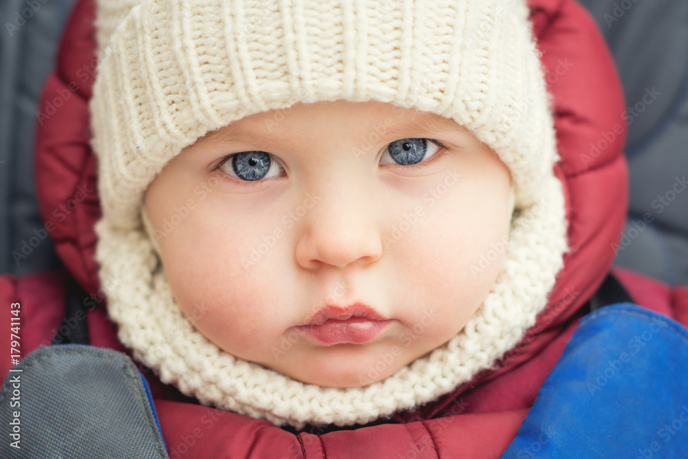 cute caucasian baby boy 2 years old in a white knitted warm hat and scarf looks seriously at the camera (expressive look of blue eyes) cute caucasian baby boy 2 years old in a white knitted warm hat and scarf looks seriously at the camera (expressive look of blue eyes)