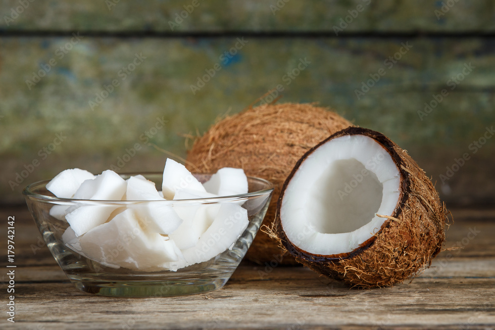 Fresh whole and cut in half coconuts with coconut shreds on wooden background with copy space
