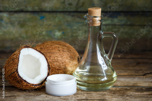 Fresh whole and cut in half coconuts with coconut oil and cosmetics cream on wooden background with copy space