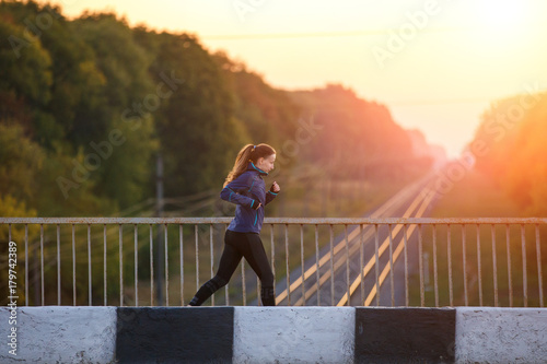 Young sporty woman jogging on bridge in the morning. Running fitness girl in sportswear outdoor image with copy space