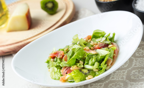 A delicious salad with salmon, lettuce, kiwi, pine nuts, Parmesan cheese. Close-up