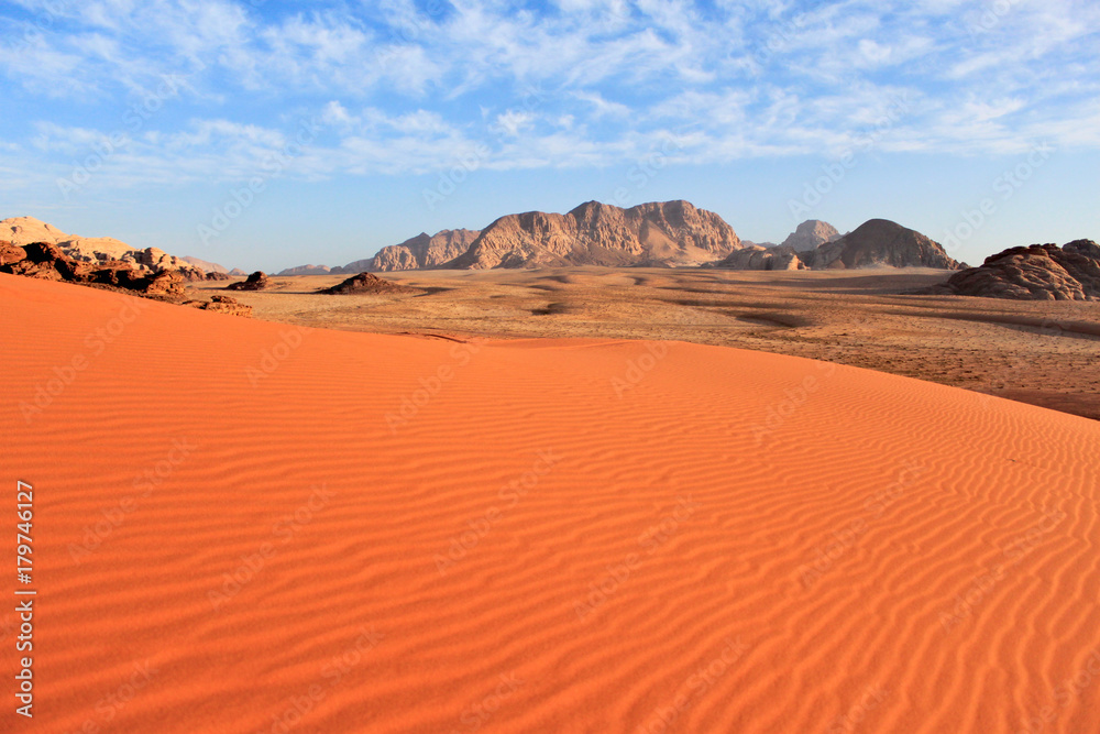 Wadi Rum desert in Jordan. Big area with smooth untouched red sand and mountains at the background and blue sky with clouds.