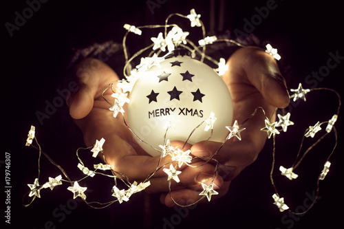 Christmas ball with the word merry xmas in man's hands. Christmas lights