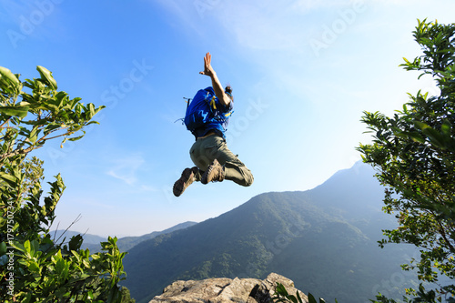 successful young woman backpacker jumping on cliff's edge