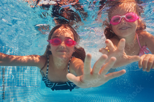 Two happy girls in goggles swimming under water