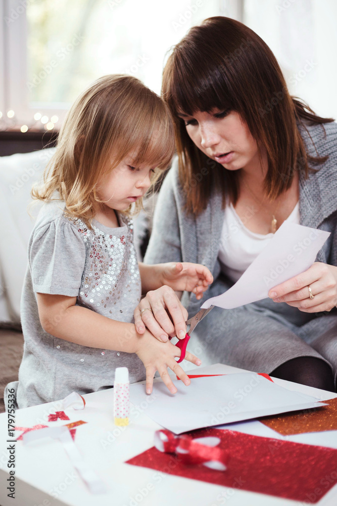 Mother and daughter making a Christmas paper chain with red and gold glitter paper. Lifestyle image, shallow depth of field.