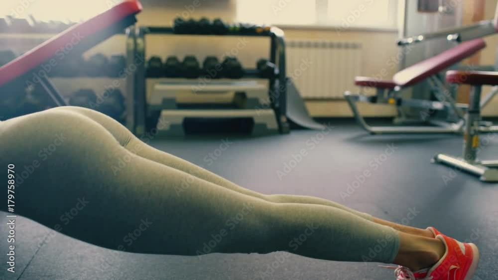 Young beautiful spotry girl with long hair doing push ups in the gym. 4 k