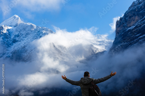Hiker with backpack standing on top of a mountain with raised hands and enjoying