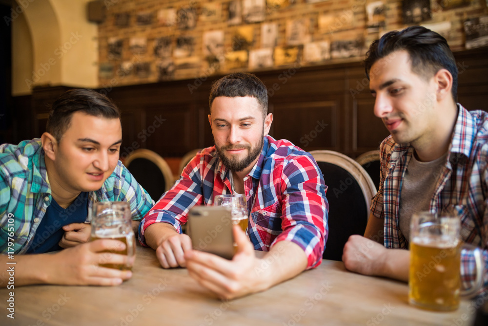 Cheerful friends having fun with smartphone and drinking draft beer in pub. Cheerful friends having fun with smartphone and drinking draft beer in pub.