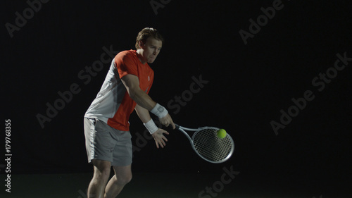 Man hitting tennis ball with racket, isolated on black