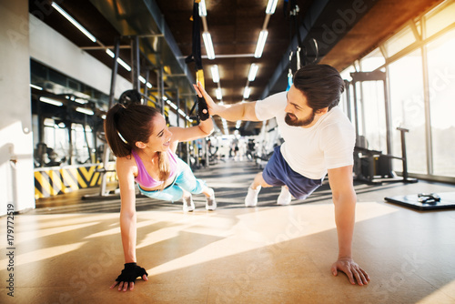 Young beautiful fitness couple smiling and clapping hands each other while doing push ups together in the gym.