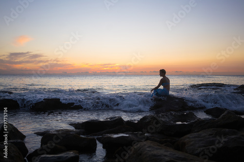 Thoughtful woman sitting on rock at beach during sunset