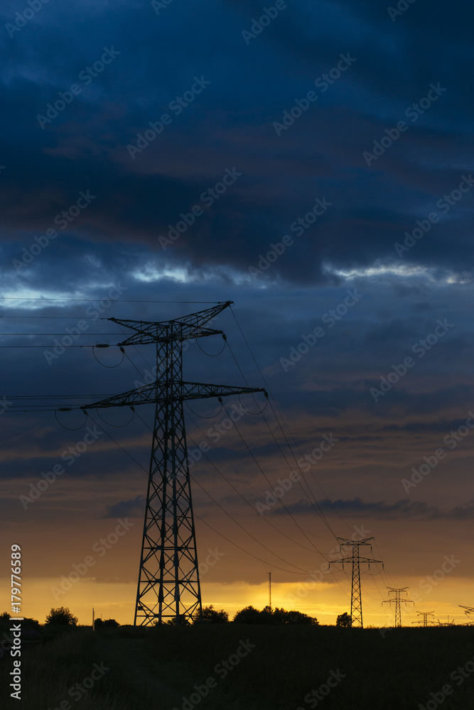 High voltage power lines and transmission towers at sunset. Poles and overhead power lines silhouettes in the dusk. Electricity generation and distribution. Electric power industry and nature concept