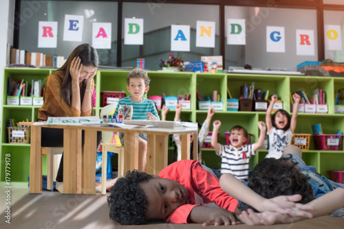 naughty preschool kids play around in class room with upset and disappointment of the teacher in dizziness acting in background photo