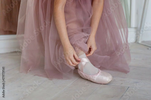 Beautiful legs of young ballerina who puts on pointe shoes at white wooden floor background, top view from above with copy space. Ballet practice. Beautiful slim graceful feet of ballet dancer photo